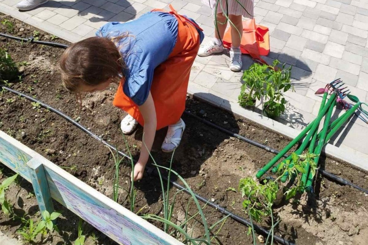Devojčica neguje biljke u bašti vrtića