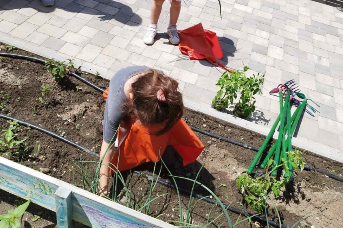 Devojčica radi sa zemljom u bašti vrtića